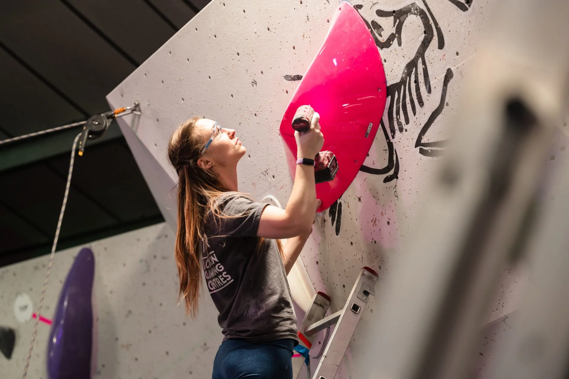 Female route-setting drilling a hold onto the wall