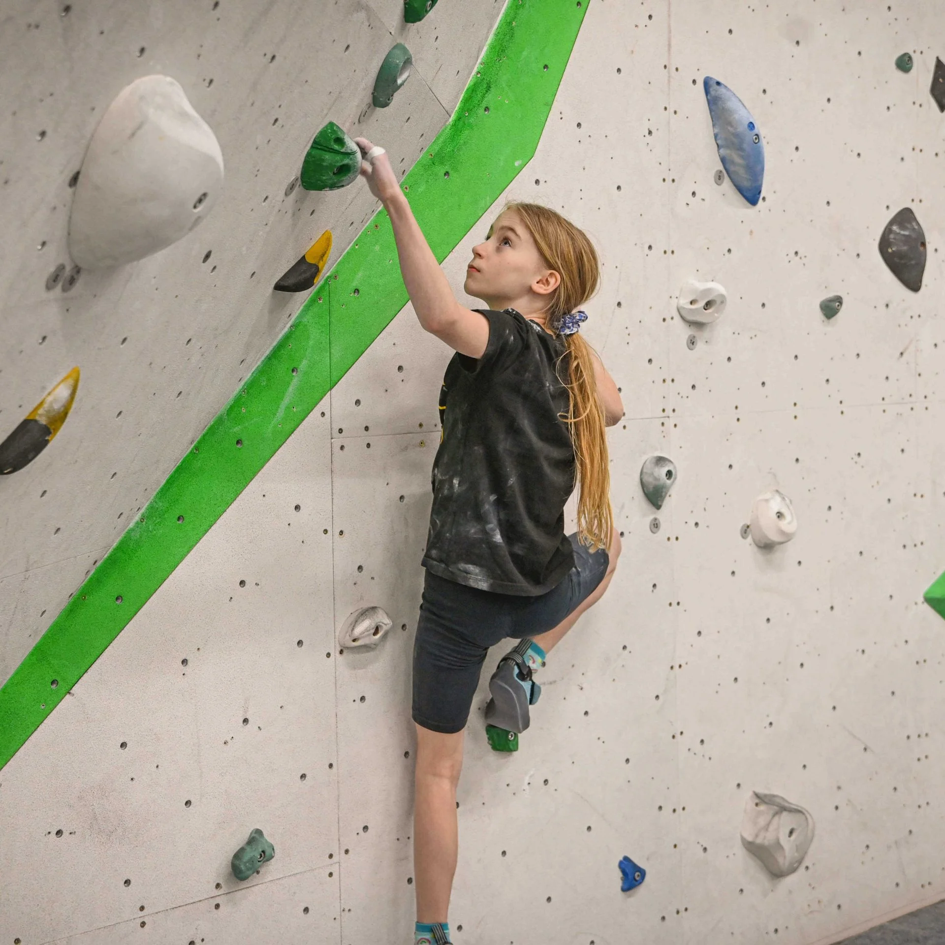 Girl climbing an indoor rock climbing wall, looking up to the next hold.